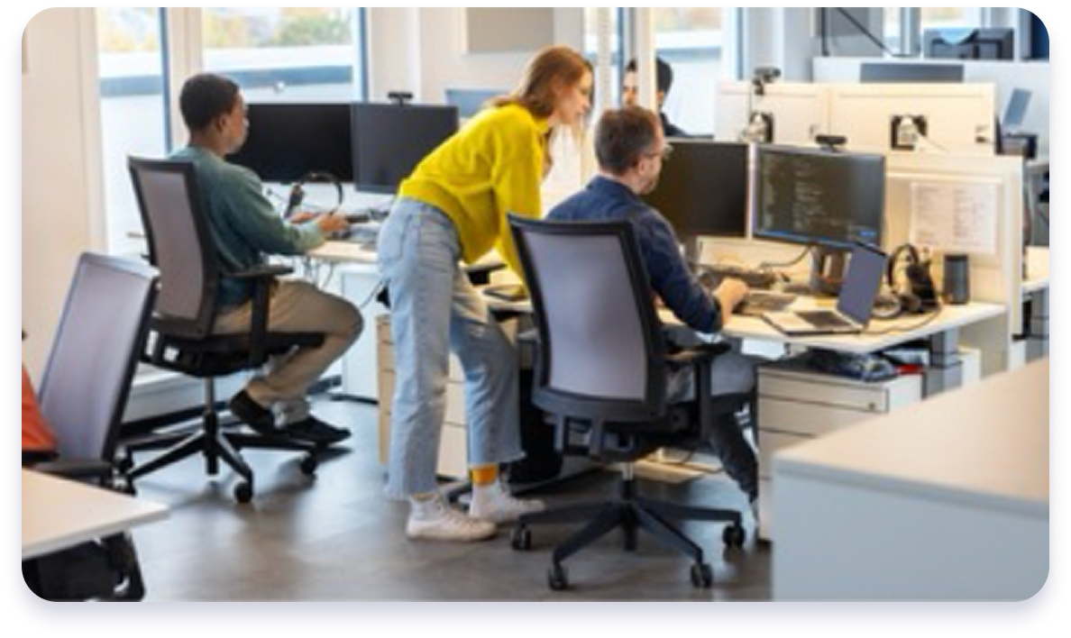 Team of developers collaborating at computer workstations in a modern office, reviewing code and digital projects together.