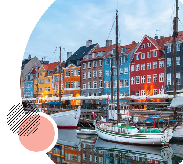 Scenic view of Nyhavn in Copenhagen, featuring colorful historic buildings along the waterfront, with sailboats docked in the canal and soft afternoon lights reflecting on the water.